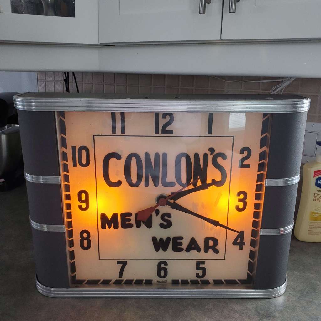 Forestville advertising clcok showing Conlon's Men's Wear on the dial illuminated